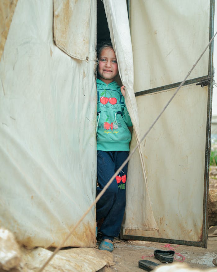 A happy child peeks out from a tent entrance in Idlib, Syria, offering a glimpse of hope.